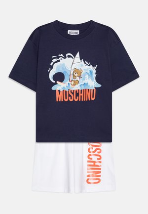 Tricou din bumbac navy cu grafică de urs și design cu placă de surf, combinat cu pantaloni scurți din bumbac albi, având textul portocaliu "MOSCHINO" pe partea laterală.