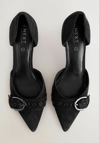 Chaussures en suede noir à bout pointu et à dos ouvert, dotées d'une large sangle avec une quincaillerie circulaire et des œillets décoratifs.