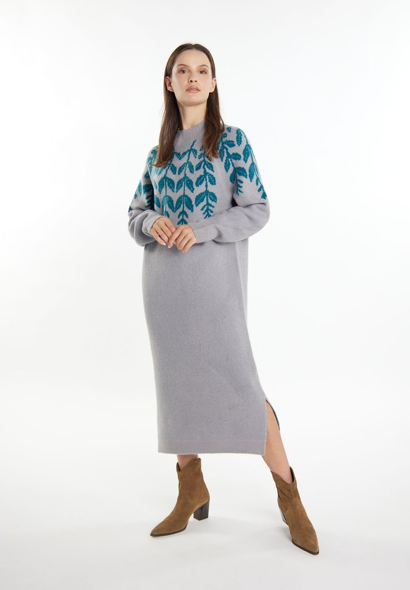 Grå sweaterkjole med teal bladmønster på skuldrene, sideslidser og lange ærmer. Bæres med brune suede ankelstøvler. Glat tekstur.