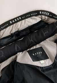 Schwarz und graue Jacke mit einer gesteppten Innenauskleidung und einem auffälligen "BAKER by TED BAKER"-Logo auf dem Kragenetikett und Riemen.