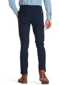 Chinos azul marino con una textura suave, bolsillos traseros con botones y un corte ajustado. Combinados con botas marrones con una suela resistente.