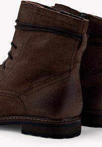 Bottes chelsea en cuir marron avec une texture lisse, fermeture à lacets et à glissière, et couture contrastante le long de la semelle et de la tige.