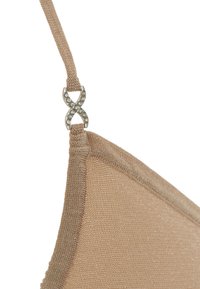 Lingerie beige con una texture morbida, caratterizzata da un accento decorativo in hardware argentato a forma di simbolo dell'infinito sulla tracolla.