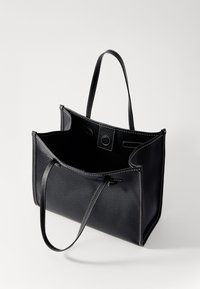 Borsa a tracolla nera in pelle con finitura texturizzata, dotata di manici sottili, apertura superiore e dettagli di cucitura beige. L'interno sembra spazioso.