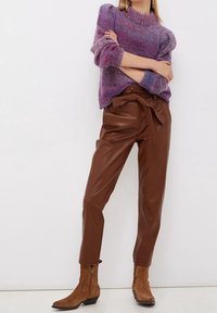 Lila und pink gestrickter Pullover mit hohem Ausschnitt, kombiniert mit braunen Kunstlederhosen mit gebundenem Bund und braunen Stiefeletten.