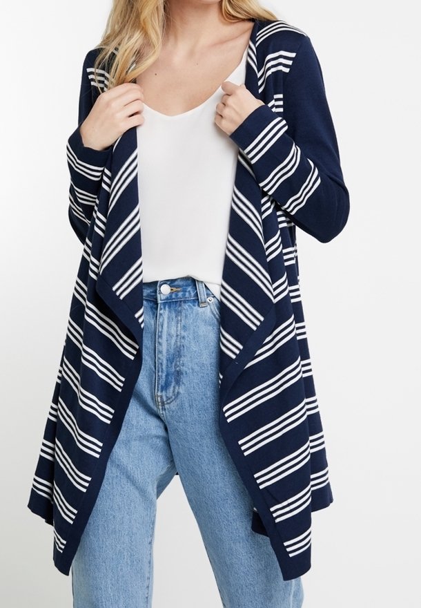 Femme portant un cardigan bleu marine à rayures horizontales blanches sur un top blanc et un jean taille haute bleu clair.