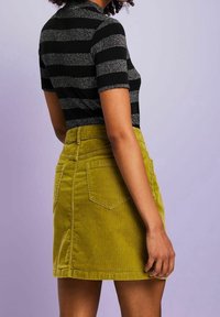Czarny i srebrny dzianinowy top w paski z krótkimi rękawami, zestawiony z zieloną mini spódnicą z aksamitu sztruksowego, posiadającą tylne kieszenie i prosty dół.