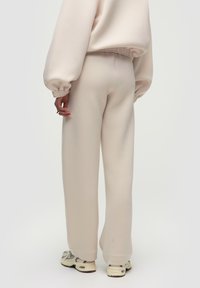 Beige, locker sitzende Sweatpants aus weichem Stoff mit glatter Textur, ausgestattet mit einem elastischen Bund und geraden Beinen. Kombiniert mit hellen Sneakers.