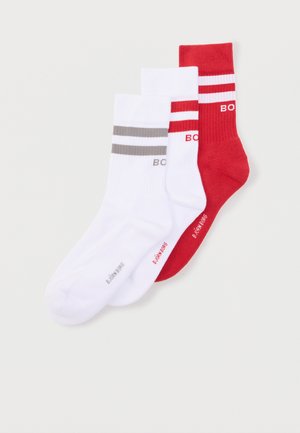 Trois chaussettes mi-mollet, deux blanches avec des rayures grises et rouges, une rouge avec des rayures blanches, toutes avec le logo "BOSS" sur les poignets.