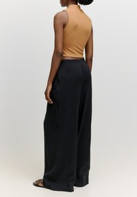 Rippentop ohne Ärmel in Beige, kombiniert mit fließenden, hochgeschnittenen, schwarzen weiten Hosen. Das Outfit zeichnet sich durch eine glatte Textur und ein minimales Design aus.