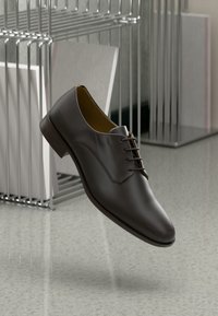 Scarpa in pelle marrone con finitura liscia, caratterizzata da un punta arrotondata, design con lacci e dettagli di cucitura sottile. Posizionata su uno sfondo neutro.