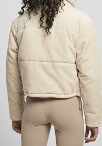 Beige kordjacka med en boxig passform, quiltat mönster och justerbar nederkant. Har hög krage och texturerad yta med ribbat detaljer.