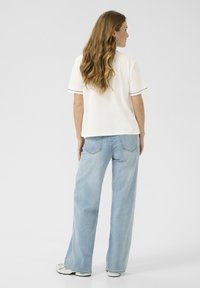 Hvid kortærmet skjorte med sort kant, parret med lyseblå vide jeans. Blødt stof, afslappet pasform og minimalistisk design.