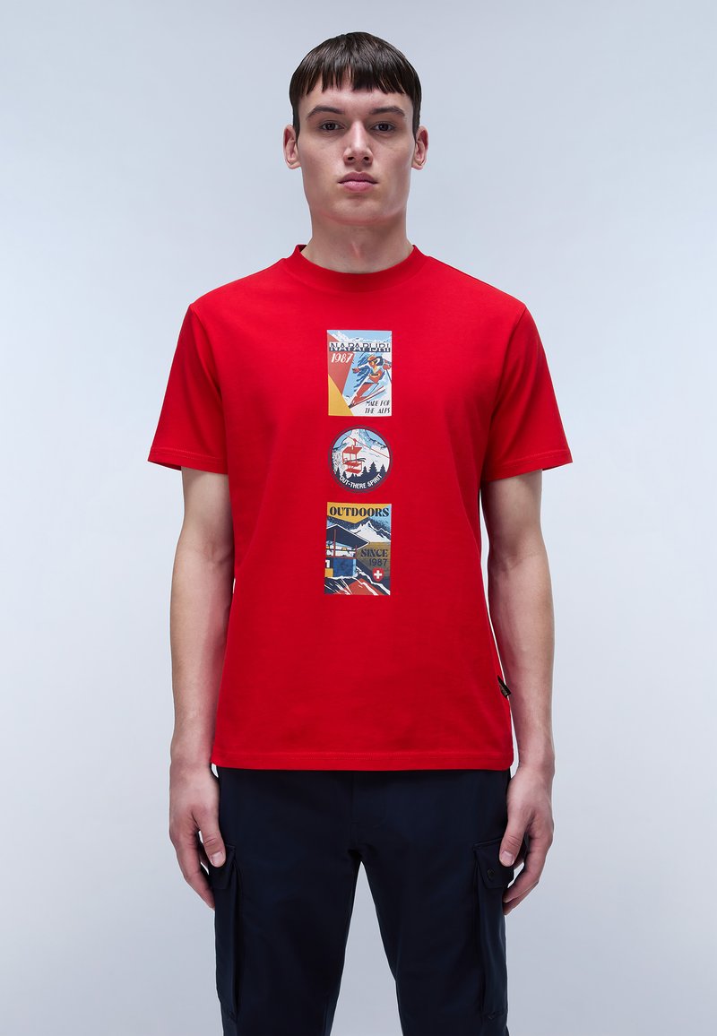 Rød bomulds T-shirt med tre grafiske lapper med udendørsmotiver og tekst, centreret på fronten. Kortærmet og med rund halsudskæring.
