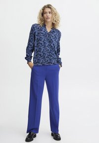Blauwe bloemenblouse met lange mouwen en een kraag, gecombineerd met wijde blauwe broeken. Gladde stof, gedetailleerde print en een relaxte pasvorm.