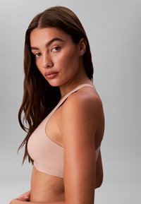 Lyserød sømløs bralette med brede stropper og en glat tekstur, der har et enkelt, minimalistisk design uden synligt hardware.
