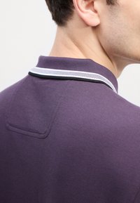 Πολυτελές μπλε πόλο πουκάμισο με υφή, με κολάρο σε λευκό και μαύρο ρίγες. Περιλαμβάνει μια διακριτική λεπτομέρεια με τσέπη στην πλάτη.