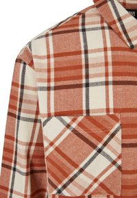 Plaid shirt in rust, cream, and black. Features a pointed collar and a chest pocket. Made of fabric with a soft texture and a checkered pattern.