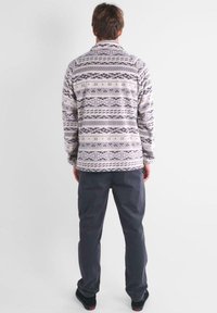 Giacca in pile con motivo geometrico in grigio e bianco; maniche lunghe, colletto e vestibilità rilassata. Abbinata a pantaloni grigi scuri e scarpe nere.