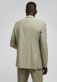 Veste de costume vert clair avec un tissu texturé, fente unique et détail de poignet à trois boutons. Conçue pour un ajustement sur mesure avec un col classique.