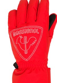Červená lyžařská rukavice vyrobená z syntetického materiálu, s výrazným logem v bílém prošívání, nastavitelným zápěstním páskem a texturovaným gripem na prstech.