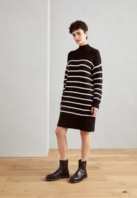 Robe pull rayée noire et crème avec des manches longues, un col montant et une texture côtelée, associée à des bottines noires.