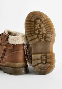 Bottes à la cheville brunes avec doublure en fourrure, présentant une fermeture éclair, une semelle en caoutchouc avec motifs de grip, et un dessus en cuir lisse.