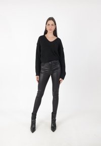 Czarny, oversize sweter z dzianiny z dekoltem w kształcie litery V, w połączeniu z dopasowanymi, czarnymi spodniami z ekologicznej skóry i czarnymi, szpiczastymi botkami za kostkę.