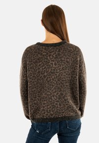 Pull en imprimé léopard dans des nuances de brun et de noir, texture douce, coupe décontractée, avec un col et des poignets côtelés sombres. Assorti à un jean bleu.