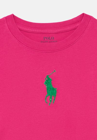 Ροζ βαμβακερό μπλουζάκι με στρογγυλή λαιμόκοψη και κοντά μανίκια. Στο μπροστινό μέρος βρίσκεται λογότυπο παίκτη πόλο με πράσινη κεντητή λεπτομέρεια.