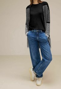 Černé tričko, převeliký kardigan se vzorem v šedých a černých odstínech, modré džíny s rovnými nohavicemi a bílé tenisky s tlumenými detaily.