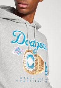 Gray hoodie featuring "Dodgers" in blue script. Displays a graphic of a championship ring with gold and blue details, along with event text.