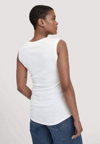 Witte mouwloze top met een aansluitend ontwerp en een zachte textuur. Heeft een ronde halslijn en gladde stof, gecombineerd met losse blauwe jeans.