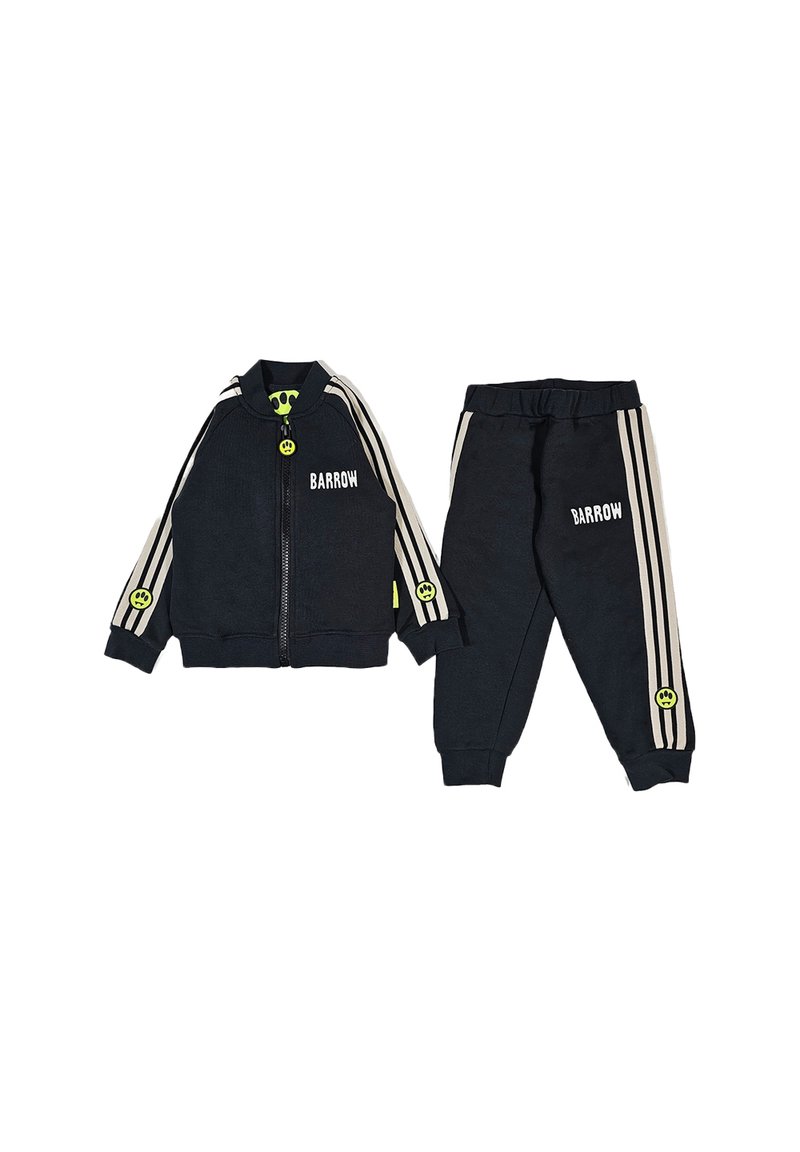 Completo tuta nera composto da giacca con zip e pantaloni, decorato con tre strisce bianche e dettagli in neon verde, incluso un motivo con un sorriso.