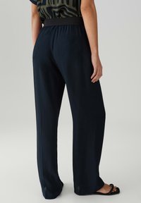 Marineblauwe wijde broek met een rekbare tailleband, een soepele textuur en zijsplitten aan de onderkant. Gecombineerd met zwarte sandalen.