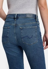 Jeans in denim blu slim fit con una sottile texture, dotati di tasche posteriori e un motivo a onda cucito. Etichetta in pelle sul passante della vita.