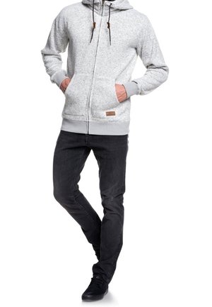 Sweat à capuche zippé gris avec deux poches avant, cordons de serrage et détail en cuir brun, associé à un jean slim noir et des chaussures noires.
