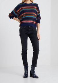 Striped knit sweater in navy, red, and blue, paired with black jeans featuring side stripes, and shiny black ankle boots.