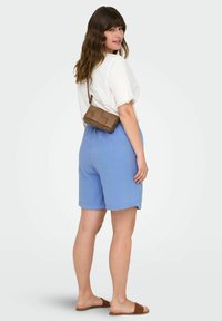 Světle modré kraťasy vyrobené z texturované látky, nošené s bílým topem s krajkovými detaily a hnědou prošívanou crossbody taškou.
