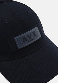 Czarna czapka baseballowa o usztywnionej konstrukcji, z teksturowaną gumową naszywką z logo "AVX" z przodu. Materiał ma gładkie wykończenie.
