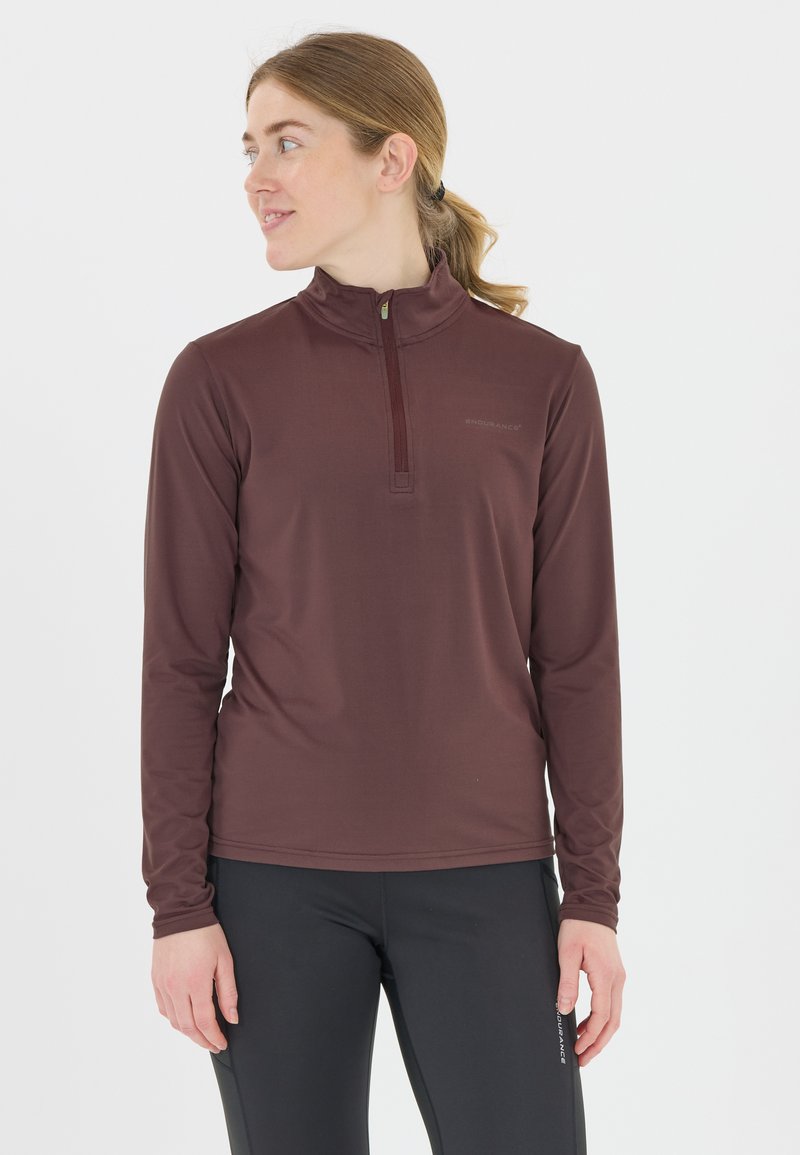 Mørkerød langærmet pullover med en kvart lynlås og høj krave. Glat tekstur med diskret branding på brystet. Bæres med sorte leggings.
