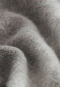 Weiche, strukturierte Stoffe in hellgrauen und beigen Farbtönen, die ein warmes, fusseliges Aussehen mit einem Strickmuster zeigen.