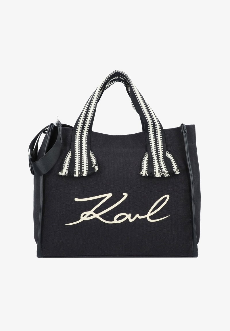 Zwarte canvas draagtas met een opvallend wit "Karl"-logo, zwart-wit gestreepte handvatten en een afneembare schouderriem.