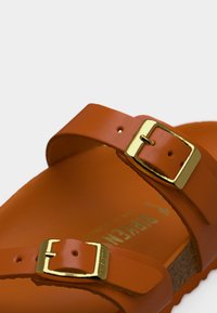 Πορτοκαλί σανδάλι με δύο ρυθμιζόμενους ιμάντες με χρυσές αγκράφες, πάτο από φελλό και υφασμένο πέλμα. Λείο φινίρισμα, μοντέρνος σχεδιασμός.