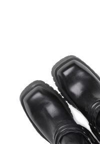Botas de cuero negro con punta cuadrada y suela de goma texturizada. Presentan detalles en metal plateado y un puño en la muñeca acanalado para añadir un toque extra.