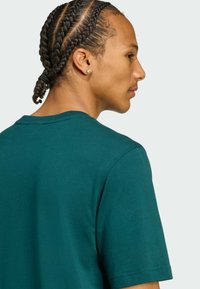 Tyrkysové bavlnené tričko s okrúhlym výstrihom a krátkymi rukávmi, s hladkou textúrou a čistým šitím, zobrazené zozadu.