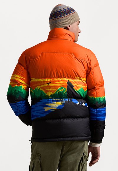 Bunte Daunenjacke mit orangefarbener Oberseite, illustriertem Landschaftsbild mit Bergen, See und der Silhouette eines Wolfes auf schwarzem Grund.