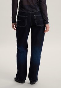 Pantaloni in denim blu scuro con finitura leggermente scolorita, cuciture bianche, due tasche posteriori e design a gamba dritta.