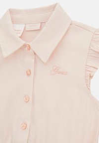 Light pink dress with a collared neckline, ruffled shoulder accents, and button-up front. Features embroidered "Guess" logo in matching pink.