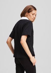 Svart t-skjorte med korte ermer og hvit krage, enkel design, myk stoff, med rett snitt og uten synlige mønstre eller dekorasjoner.